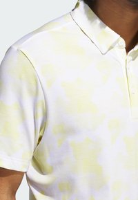 White polo shirt with a subtle yellow geometric pattern, short sleeves, and a classic collar. Fabric appears smooth and lightweight.