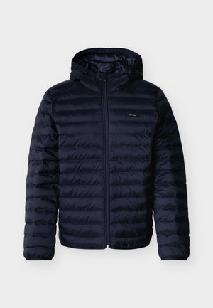 Tumma laivastonsininen toppatakki vaakasuoralla tikillä, edessä vetoketju, kiinnitetty huppu ja pieni Calvin Kleinin logo rinnassa.