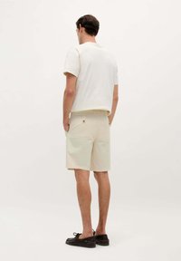 Beige bomulds-shorts med en afslappet pasform, der har sidelommer og en detalje med knap bagpå, parret med en cremefarvet kortærmet skjorte.