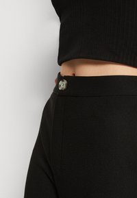 Close-up of a person wearing high-waist black ribbed pants with a marbled button and a black cropped ribbed top.