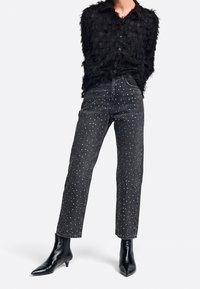 Sort fjerdetop med knaplukning, parret med højtaljede sorte jeans prydet med sølvnitter, og slanke sorte spidse støvler.