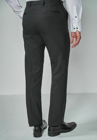 Pantalons noirs ajustés avec une coupe slim, dotés de deux poches arrière et de détails latéraux discrets, associés à des chaussures de ville noires brillantes.