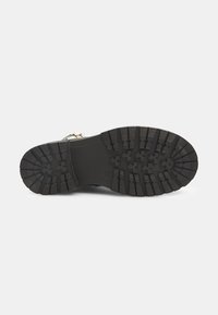 Suela de goma negra con patrones profundos para tracción. Cuenta con una superficie texturizada y ligeras ranuras; resistente y diseñada para la durabilidad.
