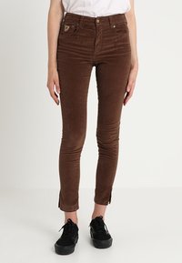 Bruna kordflors slim-fit byxor med framfickor, guldknappstängning och sidsprund vid anklarna. Kombineras med svarta sneakers.