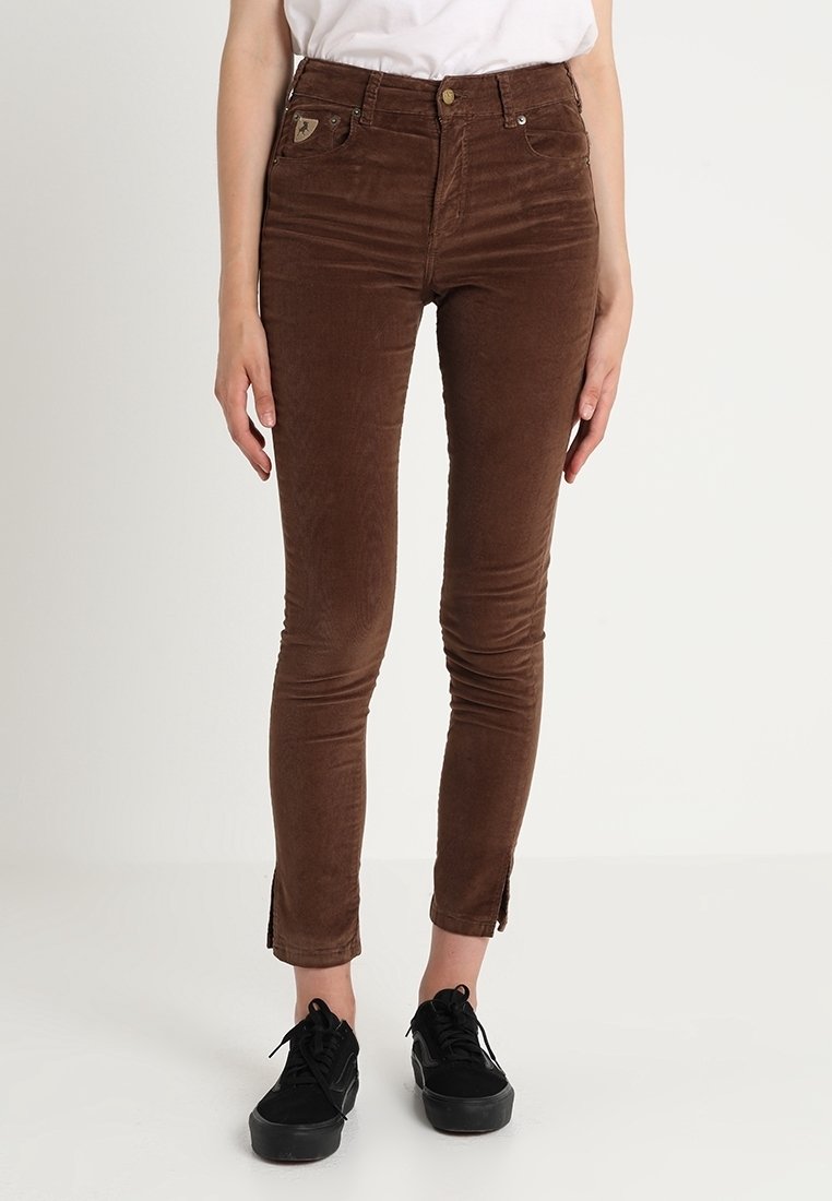 Bruna kordflors slim-fit byxor med framfickor, guldknappstängning och sidsprund vid anklarna. Kombineras med svarta sneakers.