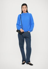 Blå genser med rund hals, ribbet mansjetter, kombinert med rette mørkeblå jeans og svarte leiligheter. Minimalistisk svart crossover-veske.