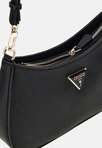Borsa nera con texture e design curvo, dotata di una zip dorata e un accento triangolare con il logo del brand sulla parte anteriore.