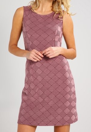 Mouwloze jurk tot op de knie met een roze en paarse geometrische geruite print, gedragen door een staande persoon met de handen in elkaar gevouwen.