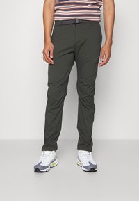 Lätta, slim-fit, mörkgröna byxor med bälte, i slät tyg och sidofickor, tillsammans med grå- och vitmönstrade sneakers.