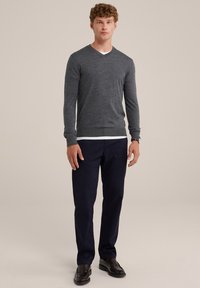 Grauer V-Ausschnitt-Pullover aus weichem Material, über einem weißen Hemd getragen, kombiniert mit navyblauen Hosen und schwarzen Slippern. Einfaches, elegantes Design.