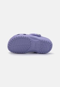 Sandal de plástico roxa com uma sola texturizada, apresentando orifícios de ventilação e uma fivela circular distintiva para fecho.