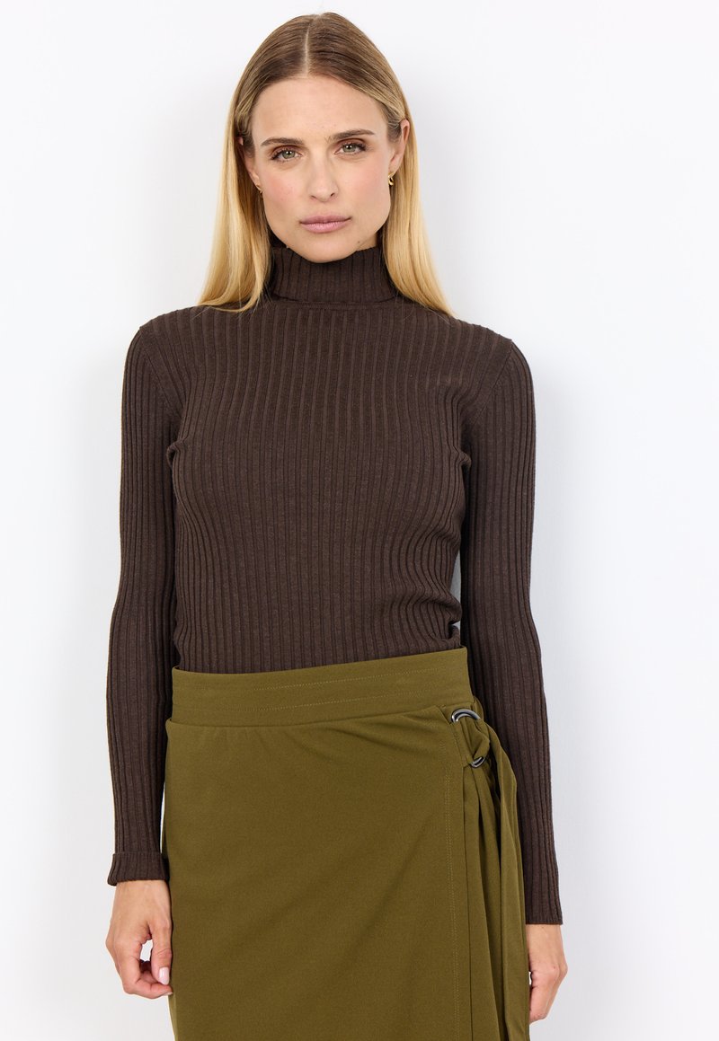 Brauner gerippter Rollkragenpullover kombiniert mit einem grünen Wickelrock mit seitlichem Ringdetail. Figurbetontes Design mit langen Ärmeln und minimaler Textur.