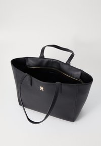 Zwarte leren tote bag, openzicht dat een ongevoerde binnenkant toont. Voorzien van dubbele handgrepen en een gouden logo-accent aan de voorkant.
