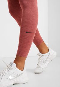 Leggings rouges chinés avec un logo Nike noir, assortis à des baskets Nike blanches avec des accents argentés. Matière lisse et extensible.