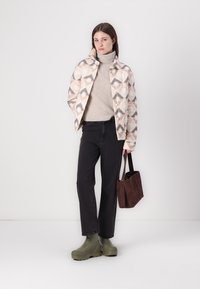 Δεμένο μπουφάν με γεωμετρικά σχέδια σε παστέλ αποχρώσεις, μπεζ ζιβάγκο, μαύρα τζιν, πράσινη υπόδηση και καφέ τσάντα.