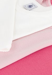Drei Baumwollbekleidungsstücke übereinander gestapelt: Ein weißes Kurzarmshirt oben, ein hellrosa Shirt darunter und ein lebhaft pinkes Shirt ganz unten.