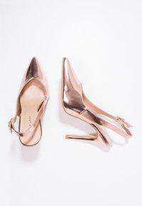 Chaussures à talons aiguilles en métal rose gold, avec un bout pointu et une finition lisse et brillante. Bride de cheville réglable et talon aiguille.