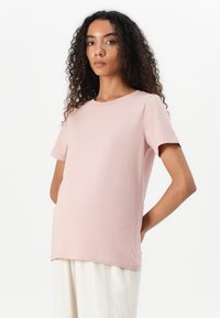 Light pink short-sleeve T-shirt made of soft fabric, featuring a round neckline and relaxed fit, worn over light-colored trousers.
