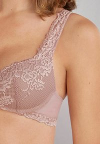 Lace-trimmed bh in zachtroze, met een textuur van gaasoverlay en gladde stof, versierd met bloemmotieven langs de banden en rand.