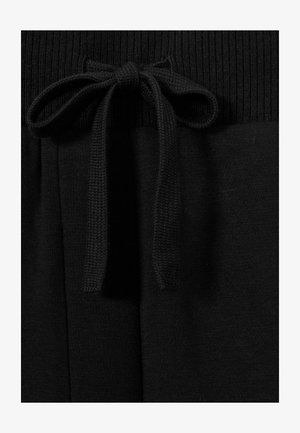 I pantaloni da jogging neri presentano una fascia in vita a coste con un dettaglio a fiocco. Il materiale è liscio con una texture morbida, e il design include delle pieghe.