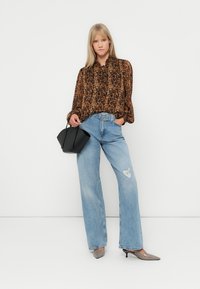 Bluza s uzorkom leopard s dugim rukavima, svijetloplave traperice visokog struka, crna torba, i sivi cipele s oštrim nosom i blagim sjajem.