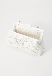 Borsa bianca con design floreale 3D, finitura lucida e accessori dorati. Presenta una chiusura a scatto e un interno foderato in tessuto.