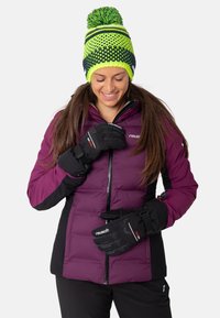 Paarse pufferjack met zwarte accenten, rits aan de voorkant, gecombineerd met zwarte handschoenen met gripontwerp. Gebreide beanie met groene en marineblauwe strepen.