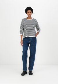 Camisa de mangas longas às riscas pretas e brancas combinada com jeans azuis de cintura alta e sapatos pretos; tecido suave, corte confortável, design minimalista.