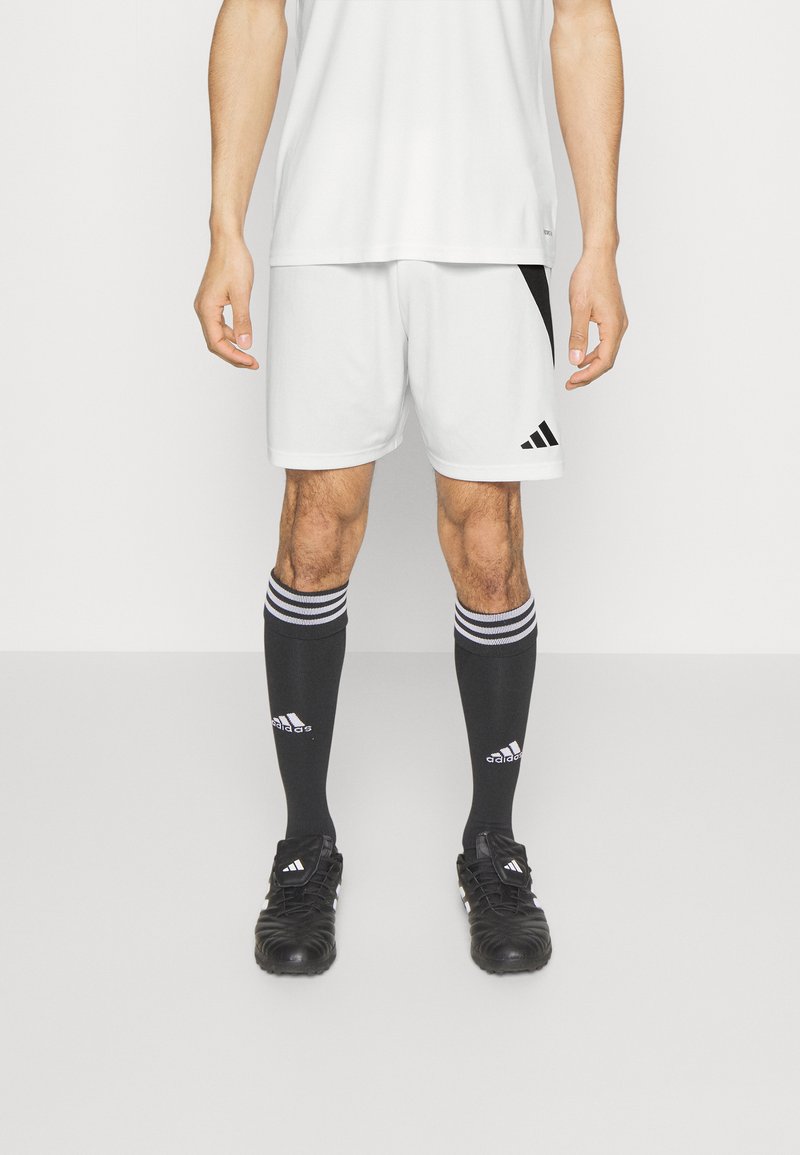 Vita sportshorts med svarta detaljer, tillsammans med knälånga svarta strumpor med vita ränder och en svart träningessko.