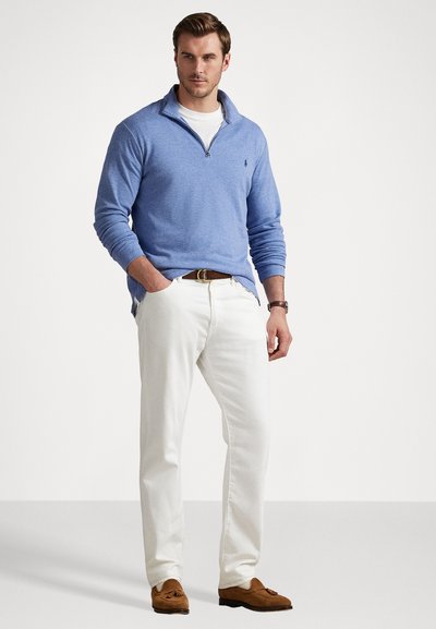 Suéter de pullover azul claro con un cuello tipo mock con cremallera, combinado con pantalones blancos y zapatos mocasín marrones. Textura suave en todo.