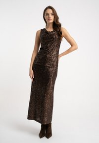 Brązowa sukienka z cekinami, z dekoltem typu wodospad, dopasowanym topem i długą spódnicą, zestawiona z brązowymi botkami na obcasie. Gładka faktura z refleksyjnymi elementami.