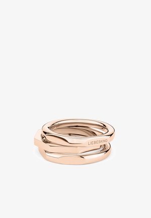 Anneaux empilés en or rose, avec une finition lisse et polie, mêlant formes arrondies et angulaires. Nom de la marque gravé et visible.