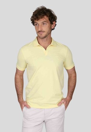 Polo shirt jaune clair avec col et manches courtes, présentant une texture subtile et une coupe classique. Le tissu semble lisse et doux.