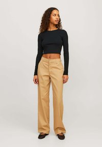 Zwarte geribbelde lange mouw crop top gecombineerd met beige wijde broek. De broek heeft achterzakken en een gladde textuur, met een getailleerde pasvorm.