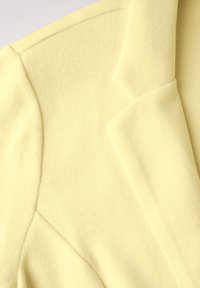 Světlý žlutý kloboukový blazer s žebrovanou texturou, strukturovanými klopami a jemným povrchem, s šikmými švy a čistým provedením.