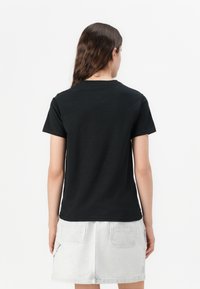 Camiseta de algodón negra de manga corta, con cuello redondo y corte recto. La parte trasera no tiene impresión y tiene una textura suave.