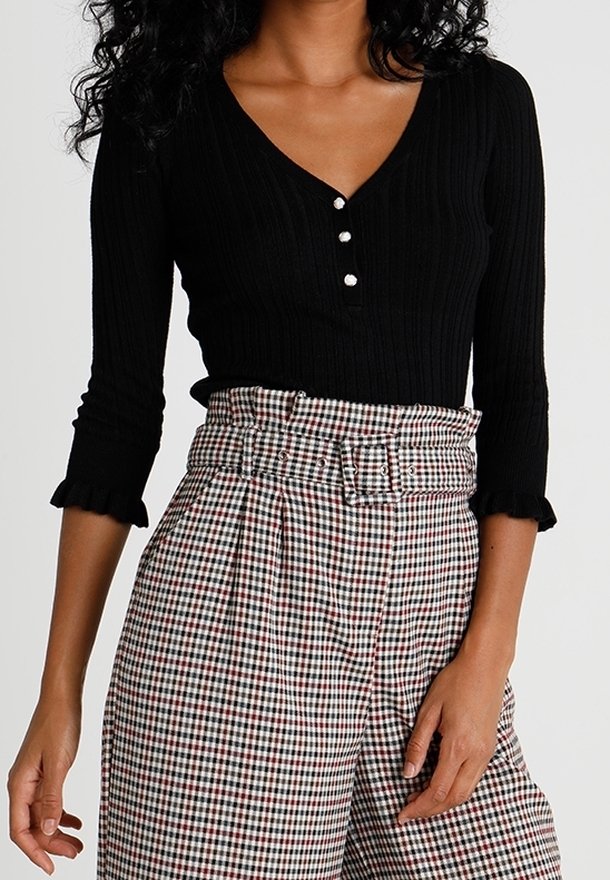 Czarny prążkowany top z dekoltem w serek i zapięciem na pięć guzików, w połączeniu z wysokim stanem kraciastych spodni z paskiem w talii i plisami.
