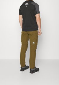 Czarna i szara koszulka z krótkim rękawem z logo, w połączeniu z khaki spodniami cargo z bocznymi kieszeniami i logo, noszone z czarnymi butami sportowymi.