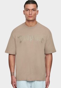 Camiseta de gran tamaño en color beige con mangas cortas, que presenta un texto gráfico en gris claro brillante que dice "Dropsis" en el pecho. Material de algodón.
