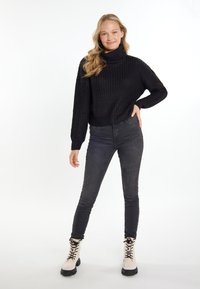 Schwarzer gestrickter Rollkragenpullover mit lockerer Passform, kombiniert mit dunklen Skinny Jeans und cremefarbenen Schnürboots mit schwarzen Sohlen.