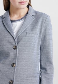 Blazer léger et texturé à motif pied-de-poule avec une coupe ajustée. Il comporte un col cranté et une fermeture à un bouton. Boutons argentés.