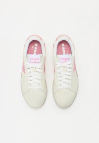 Baskets en cuir beige avec des accents roses, des lacets blancs et une languette rembourrée. Présente des perforations sur le bout et un logo à l'intérieur.