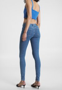 Jeans de mezclilla azul ajustados con una cintura de altura media, bolsillos traseros y un parche de cuero en la cinturilla, combinados con un top corto de punto azul.