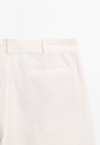 Pantaloni in lino beige chiaro con una texture liscia, dotati di una tasca posteriore singola e un design semplice e pulito.