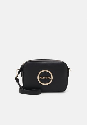 Bolso crossbody de cuero negro con logo circular dorado, cierre con cremallera y correa desmontable. Presenta una textura suave y una forma estructurada.