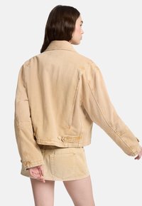 Jasnobeżowa kurtka dżinsowa o krótkim fasonie, zapinana na guziki, z widocznymi przeszyciami. Posiada tylne wstawki i oversize'owe rękawy.
