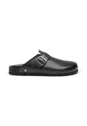 Zoccolo slip-on in pelle nera con cinturino con fibbia argento e suola testurizzata, vista laterale su sfondo bianco.