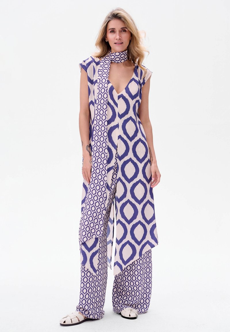 Fioletowy i kremowy kombinezon we wzory z głębokim dekoltem w serek, rękawami w kształcie kaptura i asymetrycznym krojem; zawiera pasującą choker.