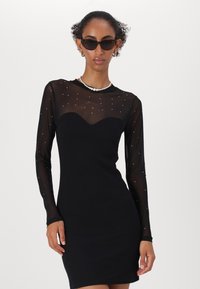 Black dress with a fitted design, long sheer sleeves adorned with small rhinestones, and a sweetheart neckline. Smooth, stretchy fabric.
