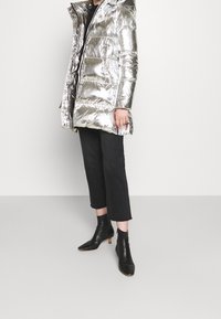 Silver puffjacka med huva, glänsande yta, framdragkedja och sidofickor. Bärs med svarta cropped byxor och spetsiga ankelstövlar.